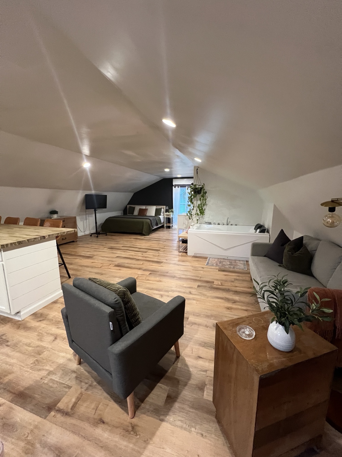 Open-plan loft with living area, king bed and soaking tub under the sloped ceiling