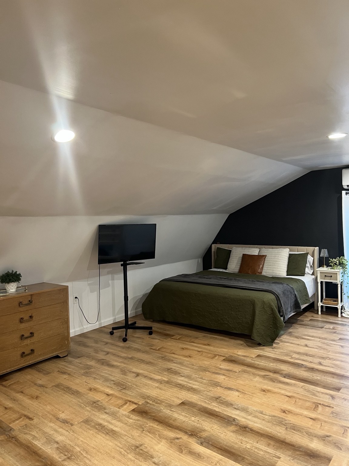 King bed with olive quilt, dresser and smart TV under the vaulted ceiling