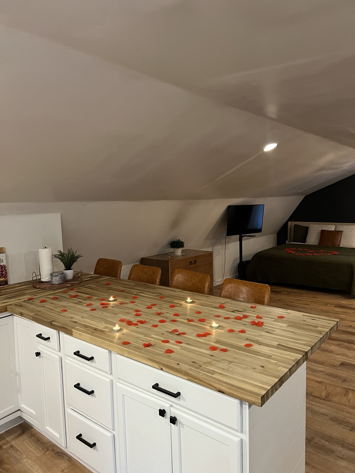 Butcher-block kitchen island scattered with rose petals, bed in the background