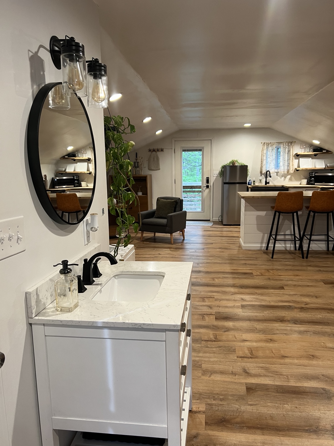 Vanity with round black mirror looking down to the kitchen and lounge chair